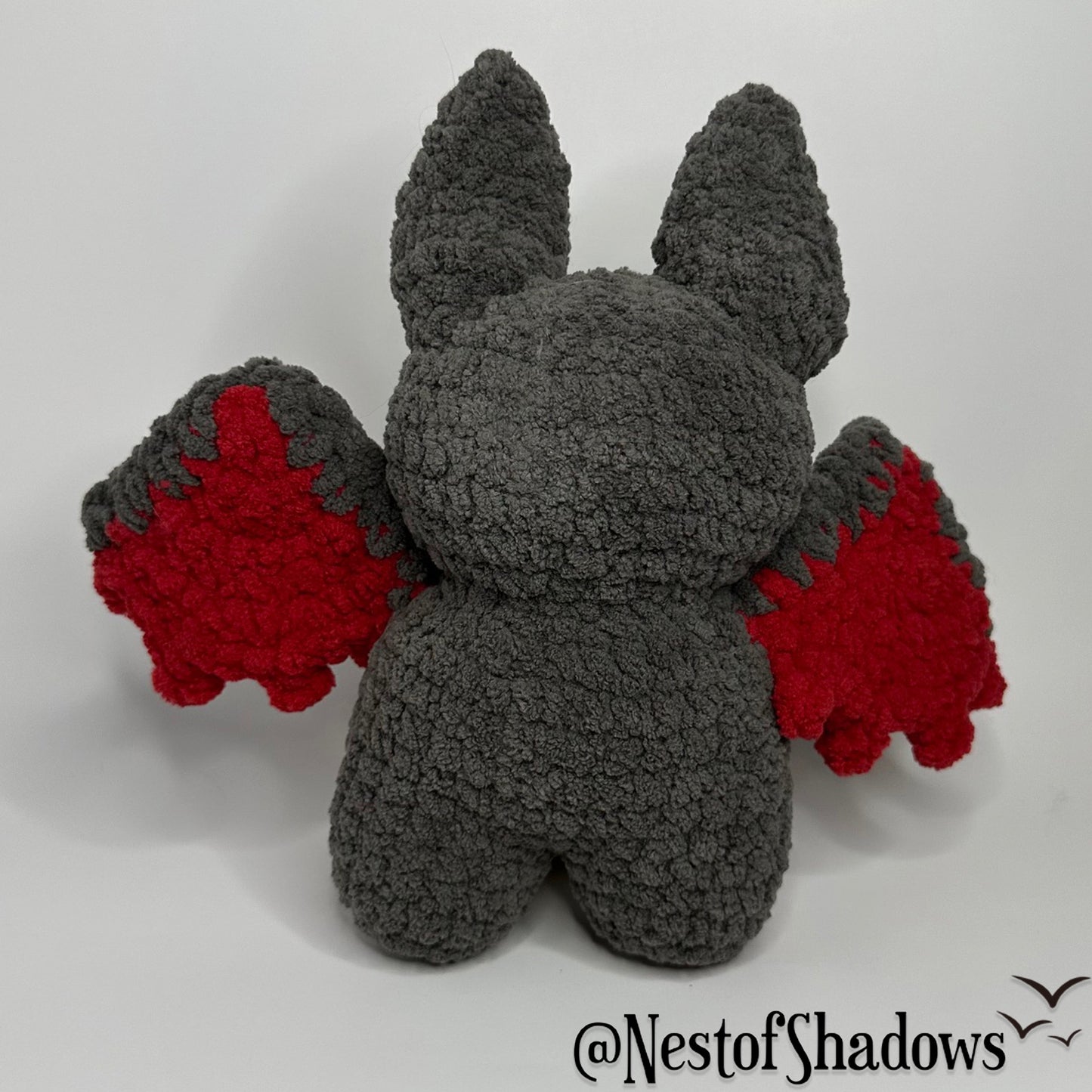 Gray and red crochet bat with a white background and Nest of Shadows watermark.