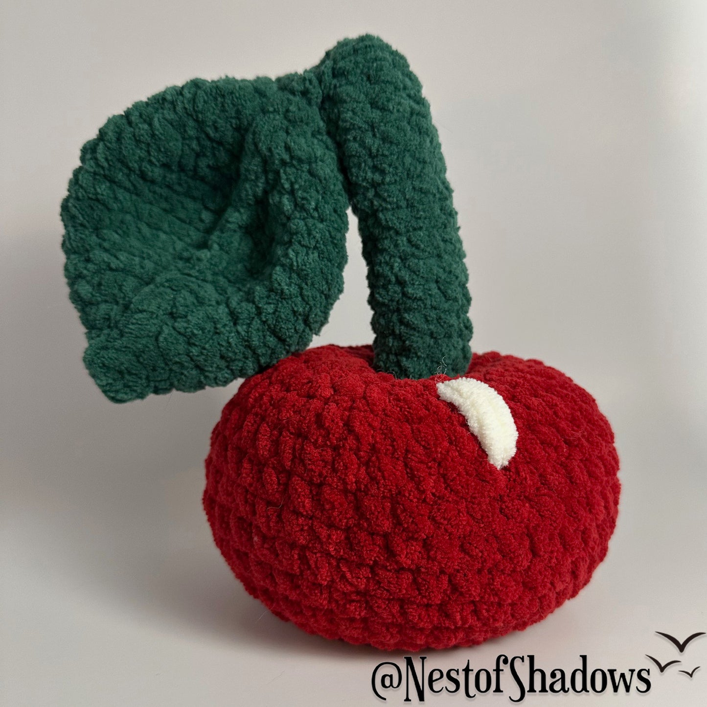 Crochet Cherry Plushie on white background. Nest of Shadows watermark.