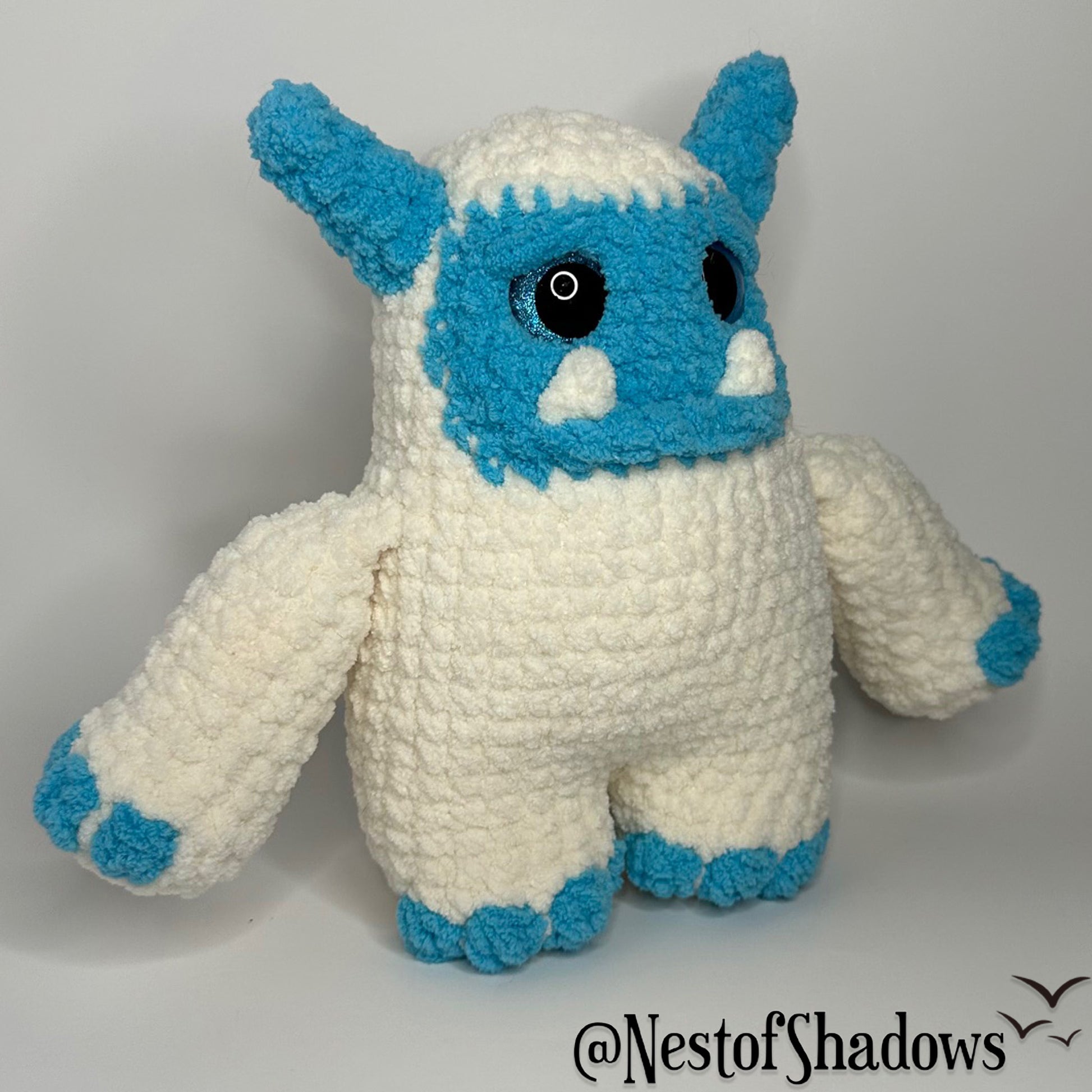 Blue and white abominable snowman crochet plushie with a white background and Nest of Shadows watermark