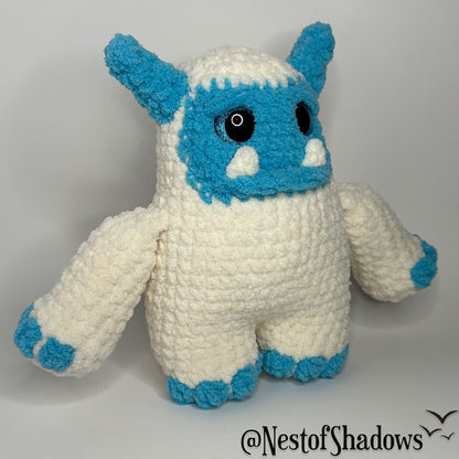 Blue and white abominable snowman crochet plushie with a white background and Nest of Shadows watermark