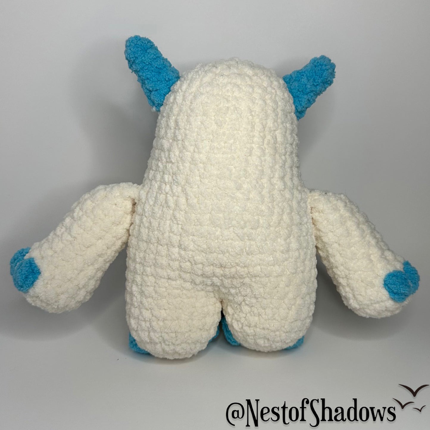 Blue and white abominable snowman crochet plushie with a white background and Nest of Shadows watermark