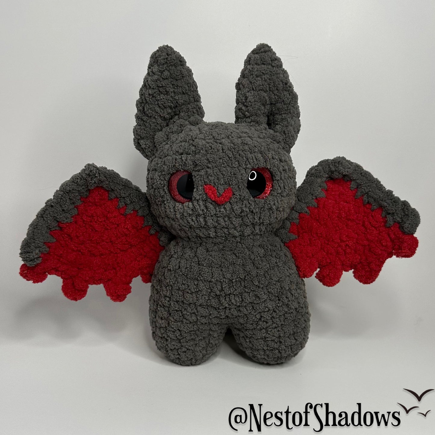 Gray and red crochet bat with a white background and Nest of Shadows watermark.