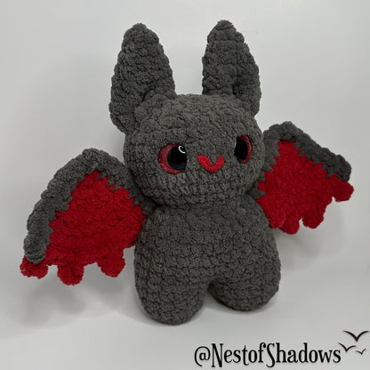 Gray and red crochet bat with a white background and Nest of Shadows watermark.