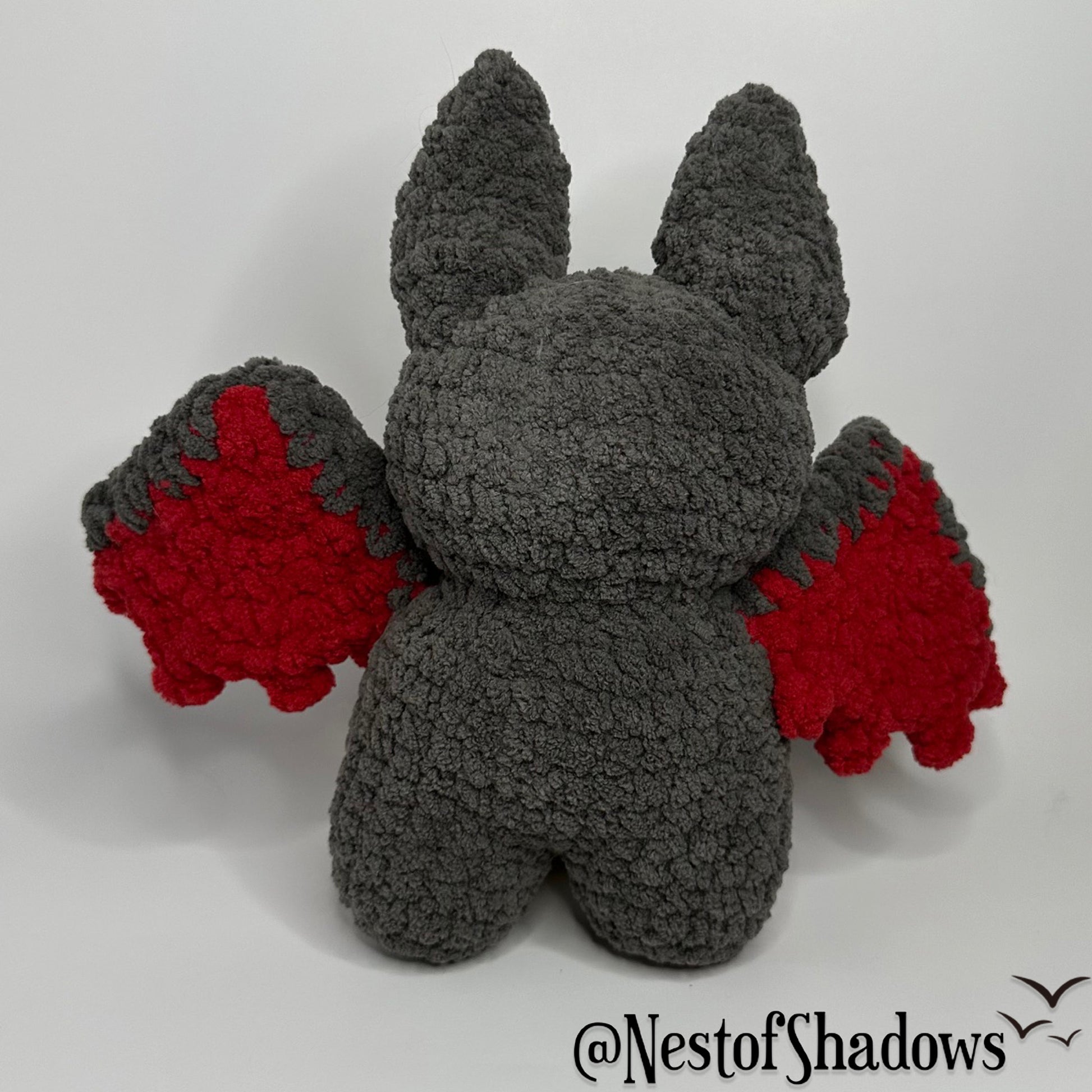 Gray and red crochet bat with a white background and Nest of Shadows watermark.