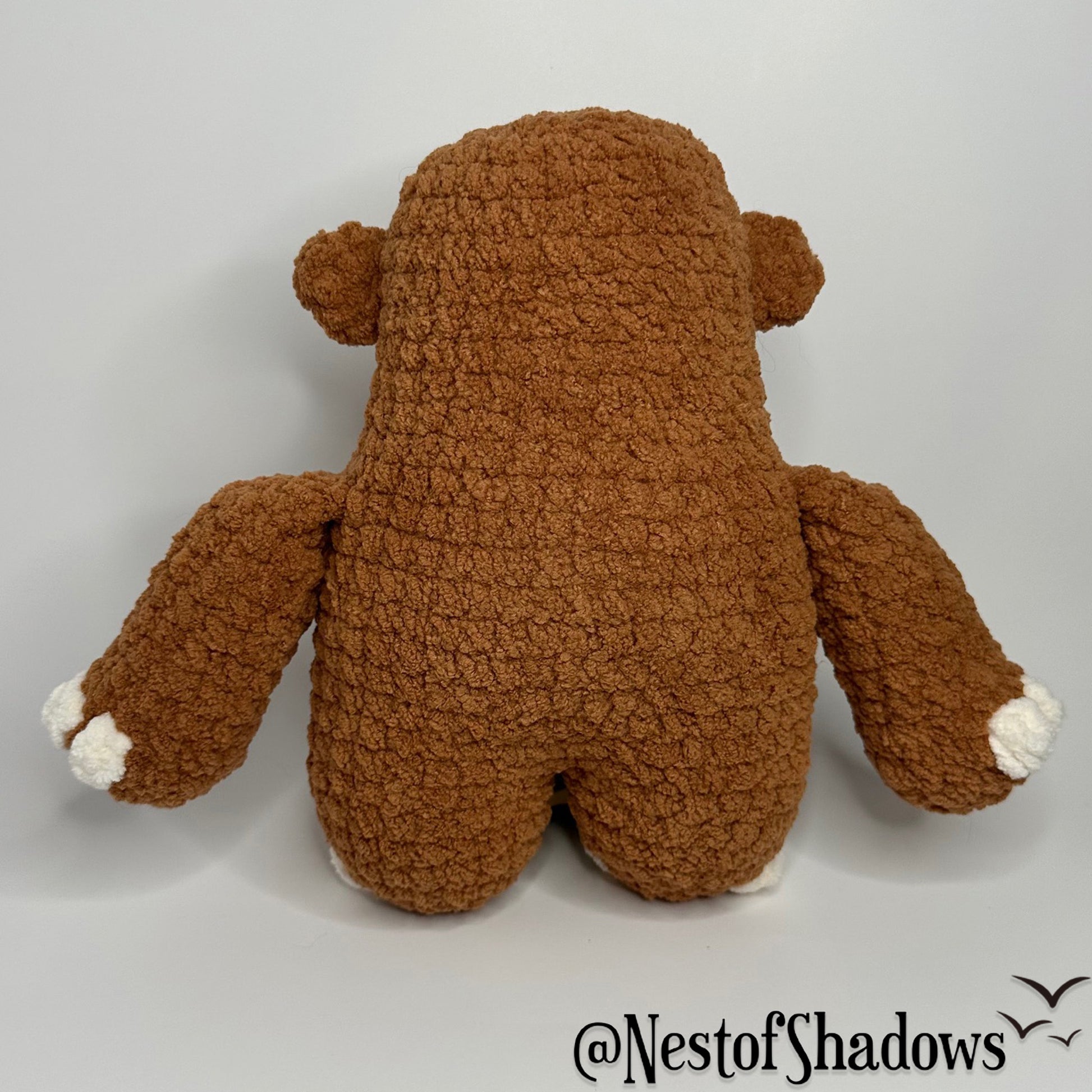 Bigfoot crochet plushie with a while background and Nest of Shadows watermark.