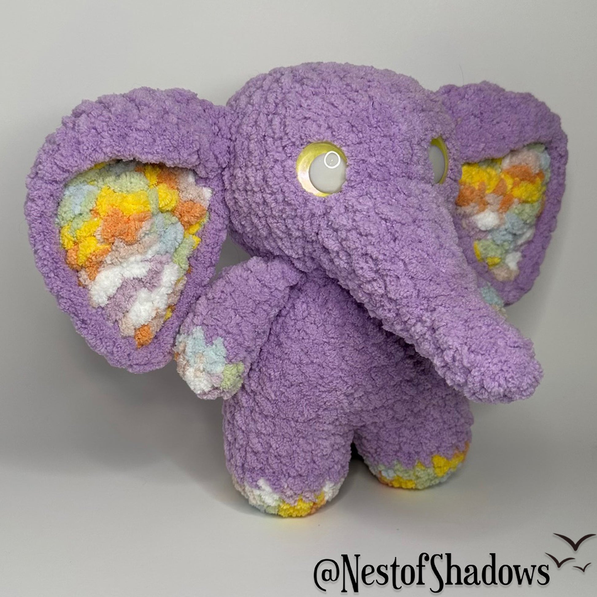 Purple crochet elephant with a white background and Nest of Shadows watermark
