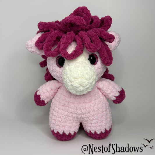 Pink pony horse crochet plushie with a white background a Nest of Shadows watermark.