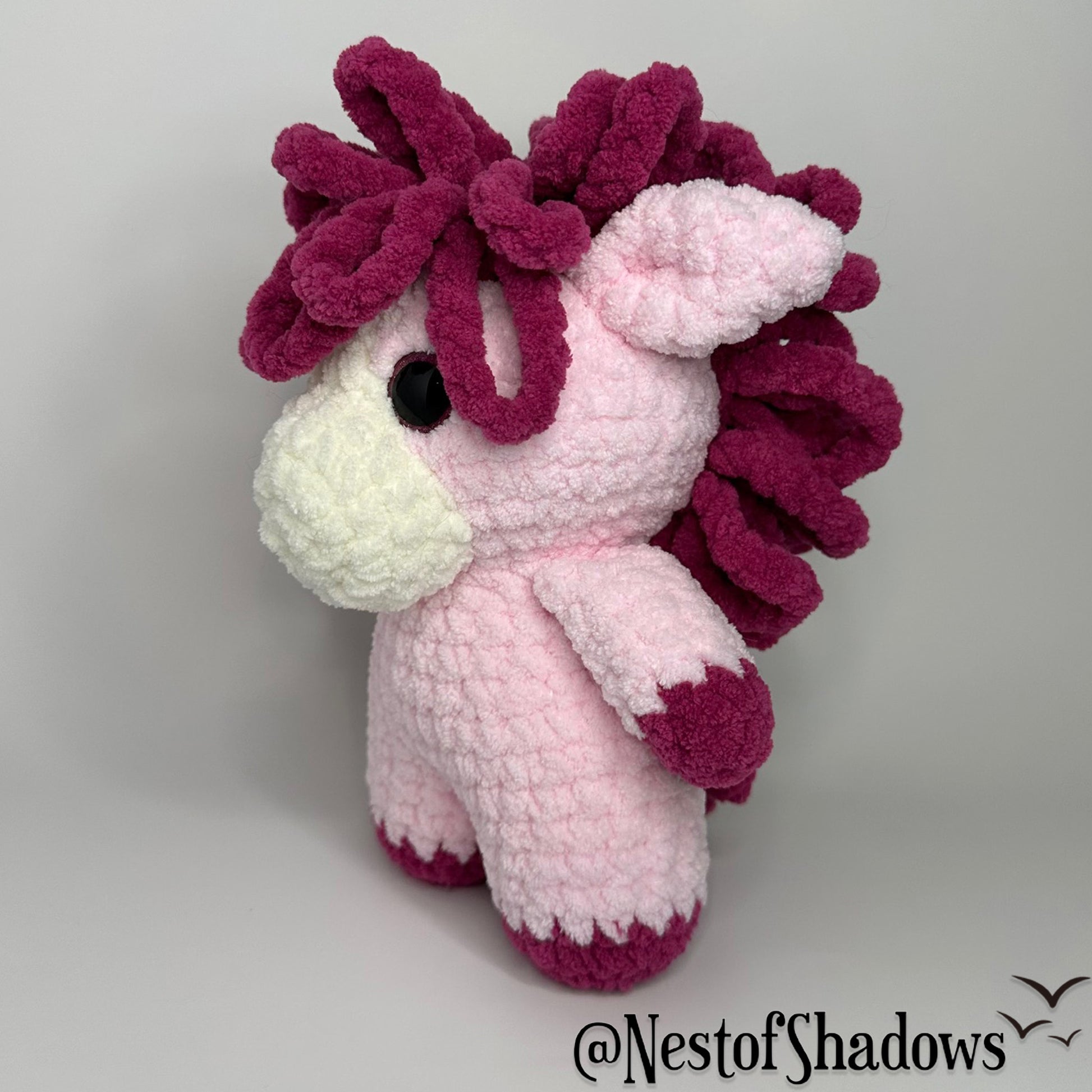 Pink pony horse crochet plushie with a white background a Nest of Shadows watermark.