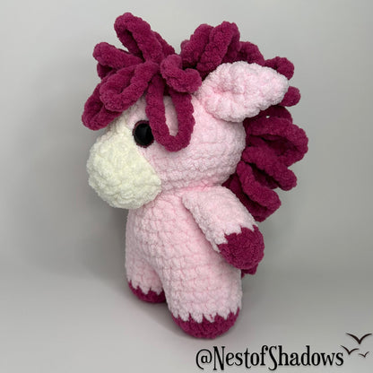 Pink pony horse crochet plushie with a white background a Nest of Shadows watermark.