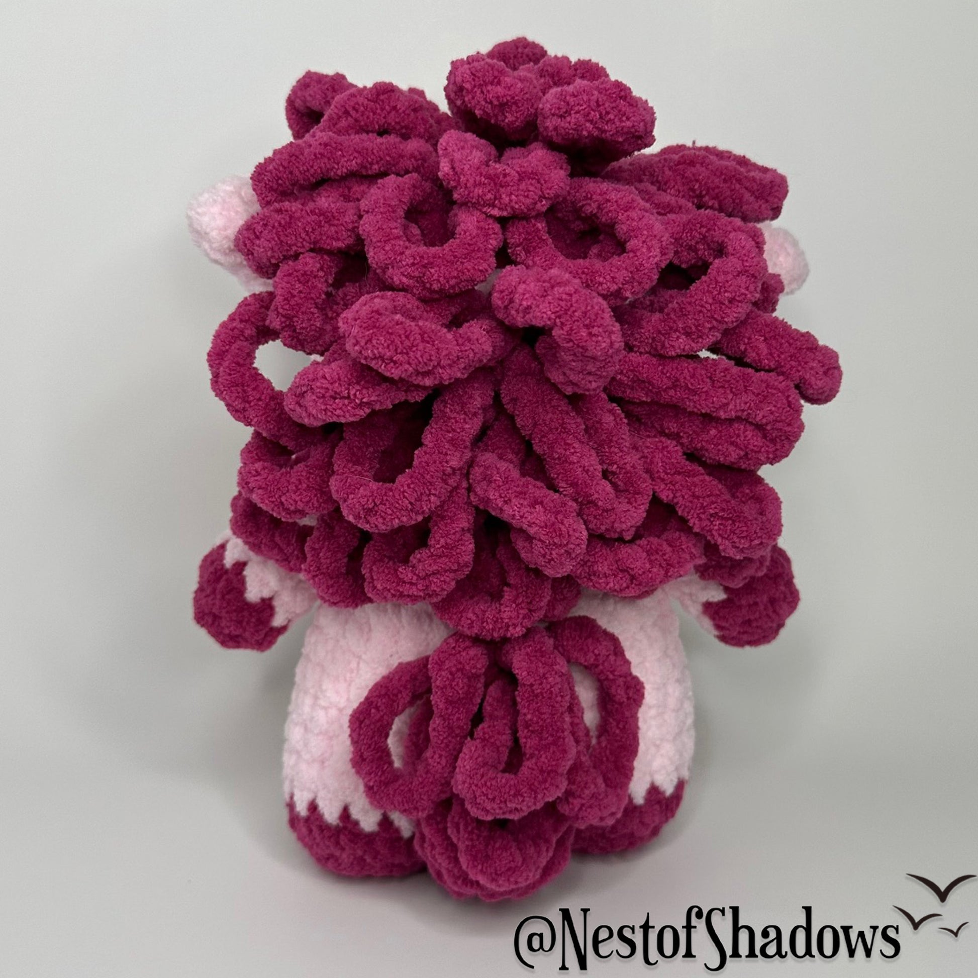 Pink pony horse crochet plushie with a white background a Nest of Shadows watermark.