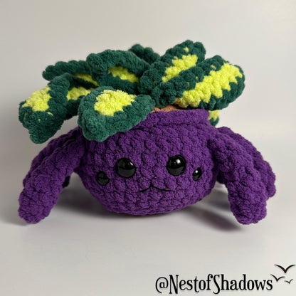 Crochet plushie of a purple spider and plant with a white background and Nest of Shadows watermark.