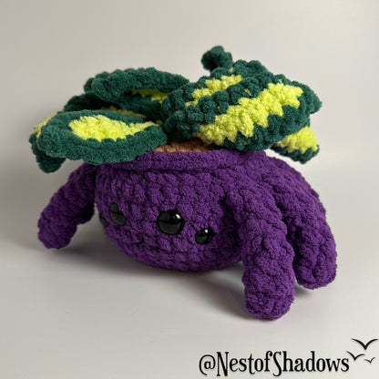 Crochet plushie of a purple spider and plant with a white background and Nest of Shadows watermark.