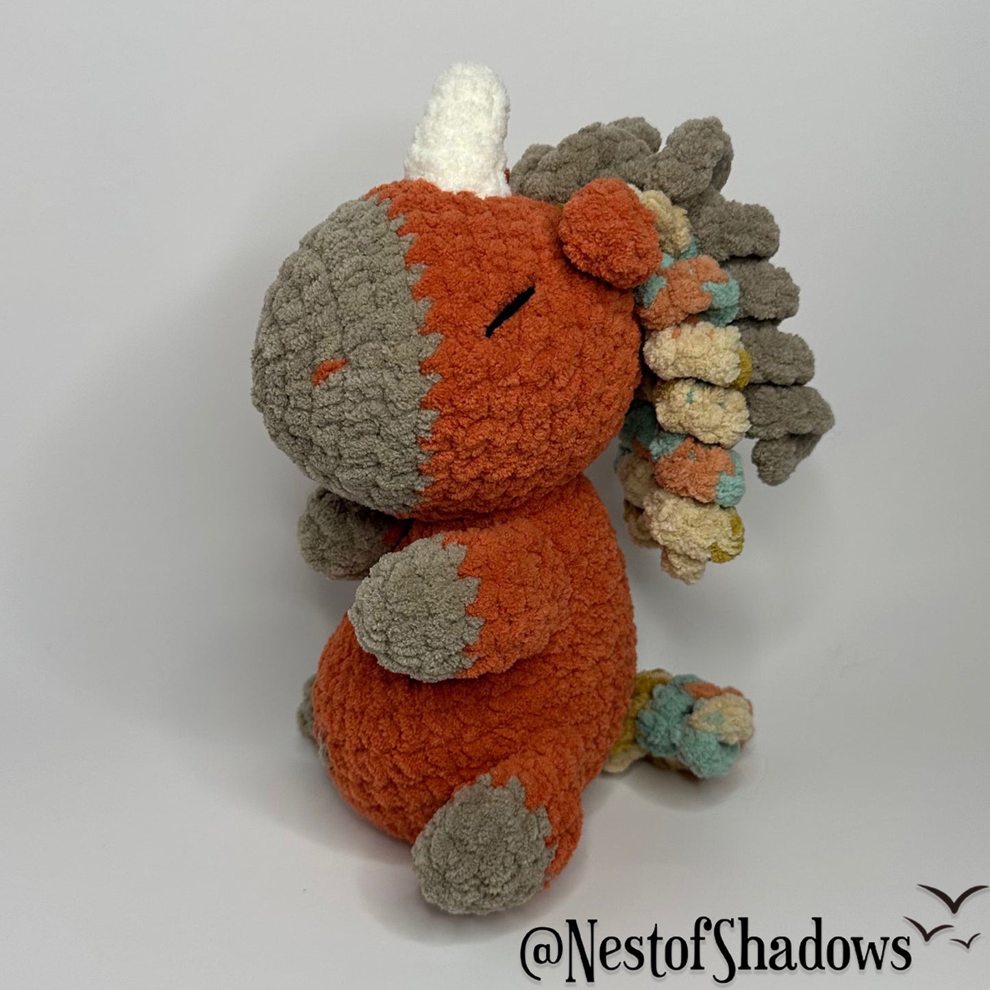 Crochet Unicorn in orange with a white background and a Nest of Shadows watermark.