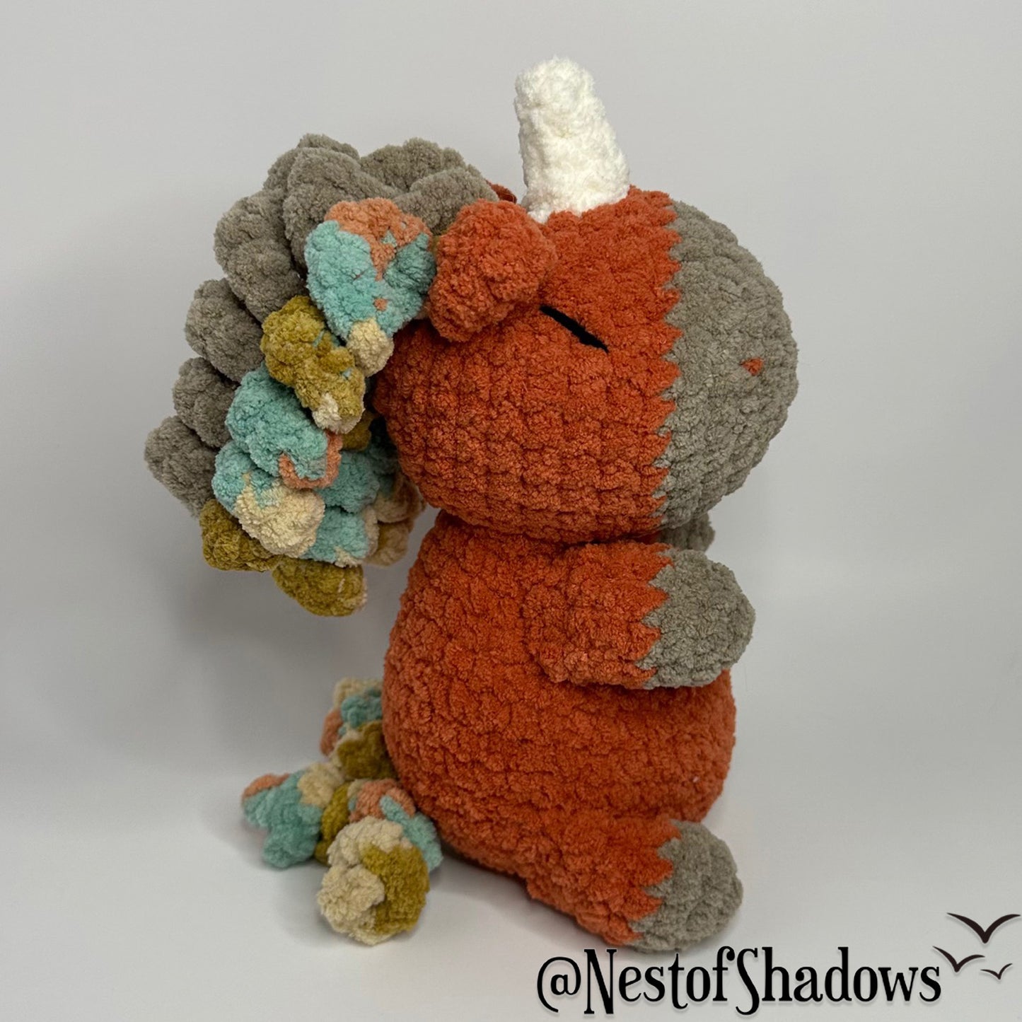Crochet Unicorn in orange with a white background and a Nest of Shadows watermark.