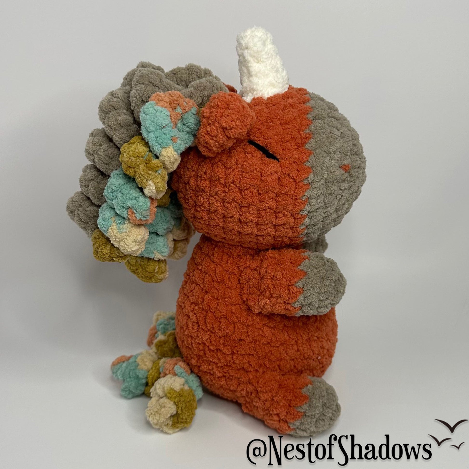 Crochet Unicorn in orange with a white background and a Nest of Shadows watermark.